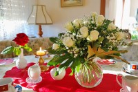 Белые розы в прозрачной вазе на красной скатерте